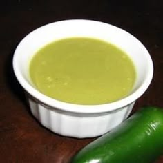 a white bowl filled with soup next to a green cucumber on a wooden table