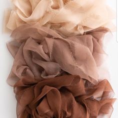 three different colors of scarfs on a white surface, one is brown and the other is beige