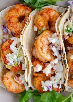 three shrimp tacos on a white plate with cilantro and cabbage garnish