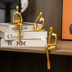 two gold figurines sitting on top of books next to an orange painting and a white mannequin