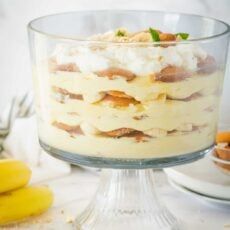 a dessert with bananas and whipped cream in the middle on a glass cake stand, ready to be eaten