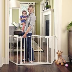 a woman holding a baby in her arms standing next to a white gate that is open