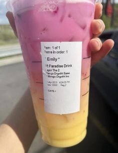 a person holding up a plastic cup filled with liquid in front of a parked car