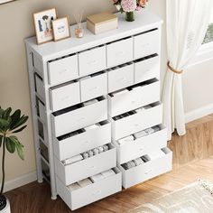 a white dresser with drawers and pictures on the top shelf next to a potted plant