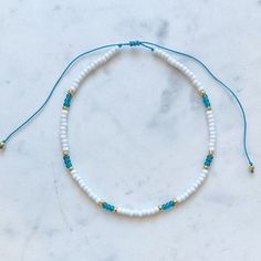 White seed bead choker necklace with an aqua/turquoise blue pattern and gold accents. Necklace length is adjustable by tightening or loosening sliding knot closure. necklace length is 13 inches fully tightened or 26 inches when fully extended. This necklace is waterproof and perfect for a day at the beach or the pool! Turquoise Tiny Beads Choker For Beach, Turquoise Tiny Beads Choker Necklace, Adjustable Turquoise Choker With Tiny Beads, Adjustable Turquoise Necklaces With Tiny Beads, Adjustable Turquoise Beaded Choker, Adjustable Turquoise Bead Choker, Adjustable Turquoise Beaded Necklace With Tiny Beads, Adjustable Turquoise Heishi Bead Necklaces, Adjustable Beaded Turquoise Choker