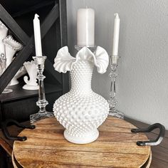 a white vase sitting on top of a wooden table next to two candles and a mirror