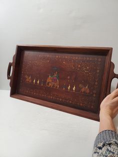 a person is holding up a wooden tray with paintings on the inside and outside it