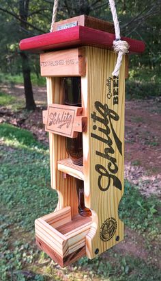 a wooden bird feeder hanging from a rope in the woods with beer bottles on it