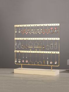 a gold jewelry rack with earrings and earring hooks on it in front of a gray wall