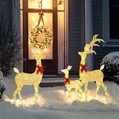 two lighted deer statues in front of a house with christmas wreath and wreath on the door