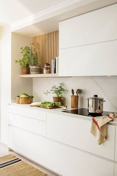 a kitchen with white cabinets and counter tops has pots, pans, and vegetables on the counters