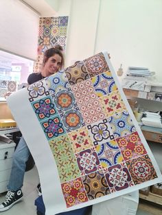 a woman holding up a large quilt made with colorful tile designs on it's sides