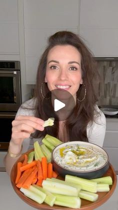 a woman holding a plate with carrots, celery and hummus on it