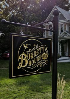 a black and gold business sign in front of a large white house on a sunny day