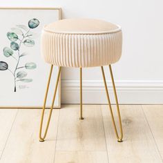 a white stool sitting on top of a hard wood floor next to a painting and a plant