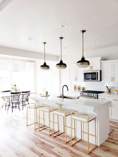 a kitchen with white counter tops and gold bar stools in front of an island