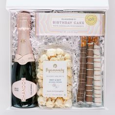 a bottle of champagne, chocolates and crackers in a gift box with a birthday cake