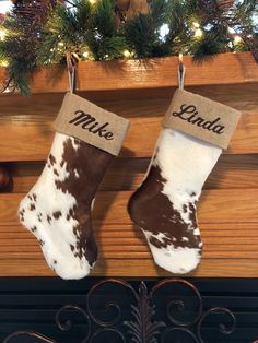 two christmas stockings hanging from a mantel decorated with brown and white cowhides