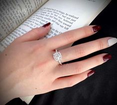 a woman's hand holding an open book with a diamond ring on her finger