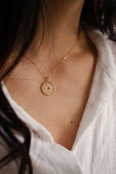 a woman wearing a white shirt and gold necklace with a small clock on it's chest