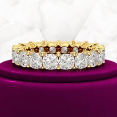 a yellow gold ring with five round diamonds on top of a purple velvet stand against a white background