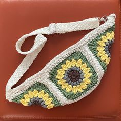 a crocheted purse sitting on top of a brown bag with a white strap