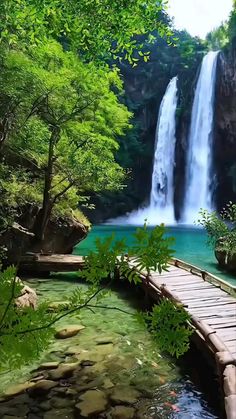 a wooden bridge crossing over a river next to a waterfall