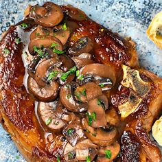 some meat with mushrooms on top of it next to garlic bread and green garnish