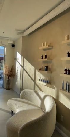 a white chair sitting in front of a window next to a shelf filled with bottles