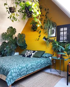 a bedroom with yellow walls and plants hanging from the ceiling, bed in foreground