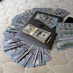 a pile of money sitting on top of a bed next to an apple laptop computer