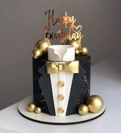 a black and white birthday cake with gold decorations on it's top, topped with a bow tie