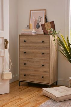 a chest of drawers in the corner of a living room with a plant on top