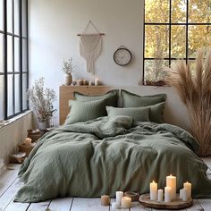 a bed with green linens and candles on the floor in front of a window