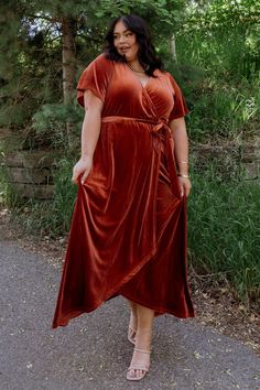 a woman in a red dress is standing on the road and smiling at the camera