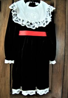 This pretty long sleeve special occasion dress has a lace trimmed collar with an oval flower design and 5 tiny white pearls in the center of the flower.  The dress also has a white lace trimmed hem and sleeves and a red satin sash that ties in the back.  The sash is held in place by a satin loop on each side. The dress opens with 5 black buttons on the back.  This dress is in excellent condition with no stains, rips or color wear.  It comes from a smoke free home and was stored between tissue pa Long Sleeve Victorian Dress For Winter Costume, Long Sleeve Victorian Dress For Fall Costume Party, Long Sleeve Victorian Dress For Costume Party, Long Sleeve Winter Costume Dress, Winter Costume Dress With Long Sleeves, Winter Costume Long Sleeve Dress, Winter Long Sleeve Costume Dress, Vintage Victorian Long Sleeve Dress For Fancy Dress, Vintage Long Sleeve Victorian Dress For Fancy Events