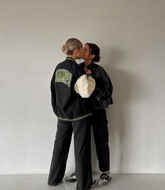 two people standing next to each other in front of a white wall and one is kissing the other