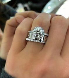 a woman's hand holding a diamond ring and two wedding bands on her fingers