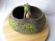 a cat bed made out of felt and yarn on top of a wooden board with a spool of thread in it