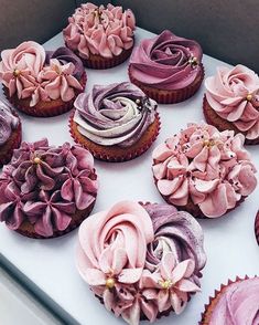 cupcakes decorated with pink and purple frosting on a white tablecloth in a box