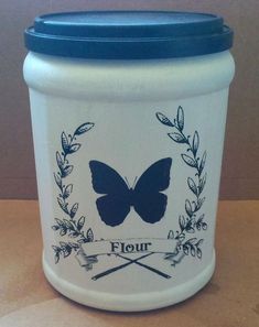 a white jar with blue lid sitting on top of a table next to a wall