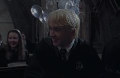 a man with blonde hair wearing a harry potter outfit and talking into a microphone in front of other people