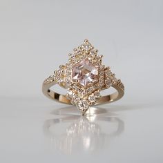 Inspired by the elegance and beauty of chandeliers, this morganite ring features a custom cut hexagon morganite center stone surrounded by natural white diamonds. Tiny white diamonds cascade down the ring band giving it a glamor effect. Made in 14k yellow gold, rose gold and white gold. This ring is handmade and designed in NYC. Materials: - 14K solid gold - 2.5 mm band thickness - 7x7mm custom cut natural hexagon morganite center stone - Natural white diamonds - SI1 clarity white diamonds. Appr Luxury Morganite Diamond Ring With Accents, Luxury Morganite Diamond Ring With Diamond Accents, Luxury Rose Gold Morganite Diamond Ring, Luxury Morganite Diamond Ring With Halo Setting, Formal Morganite Diamond Ring With Accents, Formal Morganite Diamond Ring With Diamond Accents, Luxury Morganite Jewelry With Center Stone, Luxury Morganite Diamond Wedding Ring, Blush Morganite Ring With Center Stone