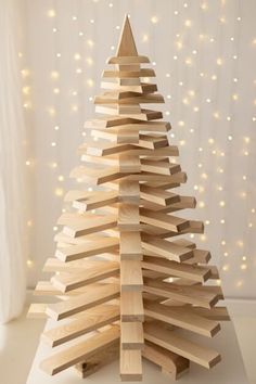 a wooden christmas tree made out of wood planks on a white surface with lights in the background