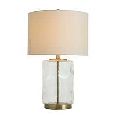 a glass table lamp with a gold base and white fabric shade on the top, against a white background