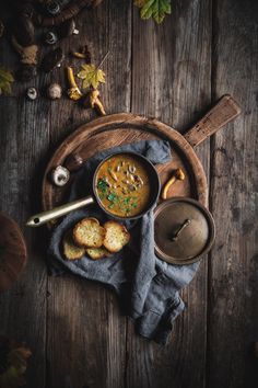 a bowl of soup and some bread on a wooden table with autumn leaves around it