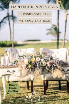 a table with flowers and candles on it in front of palm trees, surrounded by white chairs