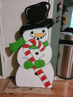 a snowman with a candy cane standing in front of a door that has a christmas decoration on it