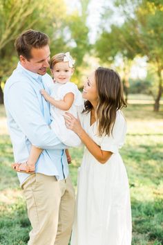 a man and woman holding a small child in their arms while standing in the grass