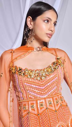 Our burnt orange 3-piece sharara set includes a peplum top, sharara, and dupatta. The peplum top features delicate embroidery with crystals, pearls, and sequins, complemented by gold metallic flowers on the front neckline and scalloped hem. The georgette sharara is adorned with crystal tassels, while the matching dupatta is embellished with scattered embroidery and finished with a delicate pearl and golden border. This ensemble offers a perfect blend of opulence and elegance. Diwali Hand Embellished Chinon Sets, Festive Hand Embellished Georgette Sharara, Festive Hand-embellished Georgette Sharara, Festive Hand Embellished Sharara For Navratri, Festival Hand Embellished Chinon Sets, Festive Hand Embellished Chinon Sharara, Anarkali Sets Hand Embellished For Festivals, Bollywood Style Hand Embellished Sharara For Festive Occasions, Bollywood Hand Embellished Sharara For Festive Occasions